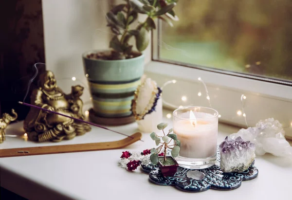 Asian money tree Crassula Ovata growing on window sill in home Feng Shui wealth and prosperity invitation altar. With smoking incense stick, laughing Buddha and crystal clusters.