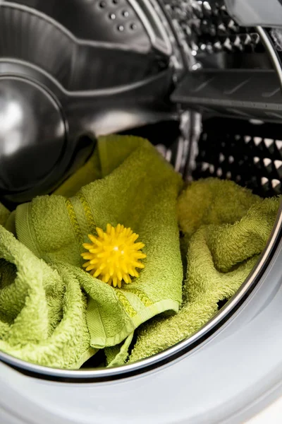 Using pvc dryer balls is natural alternative to both dryer sheets and liquid fabric softener, balls help prevent laundry from clumping in the dryer.  Woman hand put in a yellow spiky dryer ball.