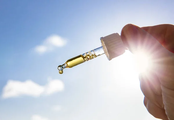Güneşli bir günde güneşe ve mavi gökyüzüne karşı güzel bir D vitamini ile el ele tutuşan damlacık pipeti. D vitamini kışın güneş yokken sizi sağlıklı tutar..