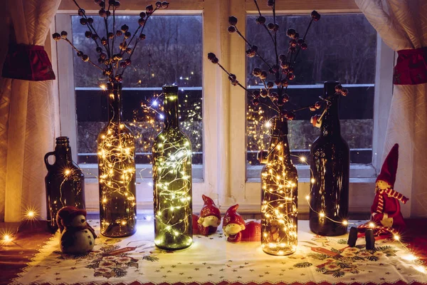精美而温暖的圣诞装潢配备了老式啤酒瓶和装满微铅派对灯的酒瓶 窗后是乡村森林 红莓瓶瓶 — 图库照片