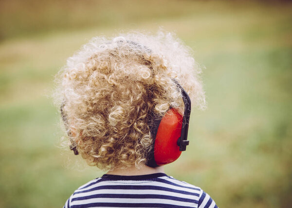 Маленький ребенок в шумоизоляционных наушниках на открытом концерте, предотвращая потерю слуха в раннем возрасте
.