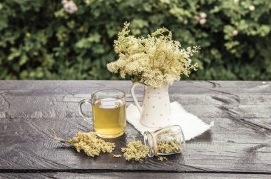 Taze Meadowsweet, Filipendula ulmaria çiçekleri vazoda ve cam içinde bitki çayı, bahçe masasında kavanozda çay tozu..