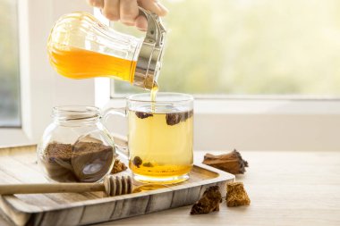 Huş ağacından gelen sağlıklı doğal doğal chaga mantarı, Inonotus oblikus parçaları cam kenarında ahşap tepside çay bardağı parçaları, güzel, güneşli arka ışık. Bal döküyorum. Bağışıklık sistemi kavramı geliştiriliyor.