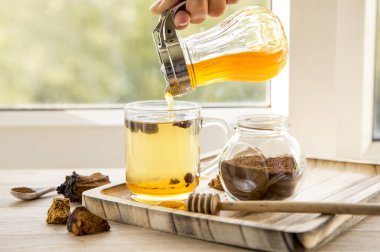 Huş ağacından gelen sağlıklı doğal doğal chaga mantarı, Inonotus oblikus parçaları cam kenarında ahşap tepside çay bardağı parçaları, güzel, güneşli arka ışık. Bal döküyorum. Bağışıklık sistemi kavramı geliştiriliyor.