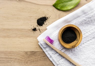 Tahta bardakta çiğ kömür tozu ve yanında da doğal bambu diş fırçası, yeşil yaprak ve banyo havlusu. Kömür diş macunu konsepti. Bir sürü kopyalama alanı.