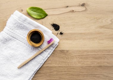 Tahta bardakta çiğ kömür tozu ve yanında da doğal bambu diş fırçası, yeşil yaprak ve banyo havlusu. Kömür diş macunu konsepti. Bir sürü kopyalama alanı.