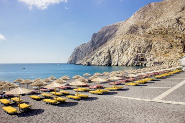 Kamari Köyü 'nün Yunan adası Santorini' deki güzel siyah kumsal, güneşli bir sabah. Bir sürü güneş şezlongları ve saman güneş şemsiyeleri. Turizm merkezi kavramı.