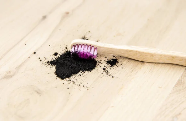 Raw activated charcoal powder on wooden background natural bamboo toothbrush inside it. Charcoal toothpaste concept. Minimalist composition with lot of copy space.