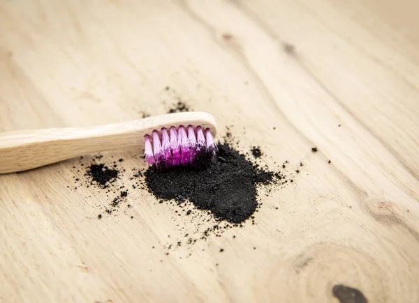 Raw activated charcoal powder on wooden background natural bamboo toothbrush inside it. Charcoal toothpaste concept. Minimalist composition with lot of copy space.