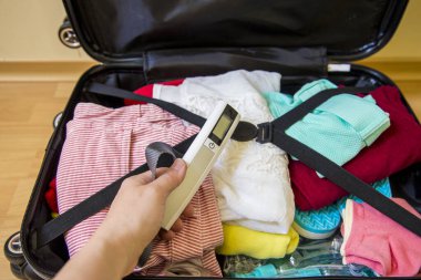 Havaalanı konseptinde aşırı kilolu bagajlardan kaçınmak için bagaja dijital bavul koyan bir kadın. Yolculuk stresini azaltır.