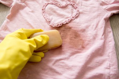 Removing stains with bile( gall, sap) soap bar. Natural chemical free household clothing washing products concept. Hand holding soap bar and rubbing removing stain from pink blouse. clipart