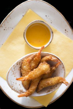 Tabağında bir kase sos olan büyük, lezzetli karideslerin üst görüntüsü, portakal sosu..