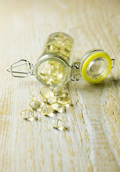 Close up of nice yellow vitamin D capsules and a glass jar with capsules on background, on wooden background.