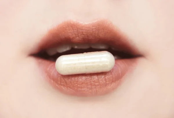 Happy woman holding a medical capsule between her lush lips. Taking medication concept, low depth of field.