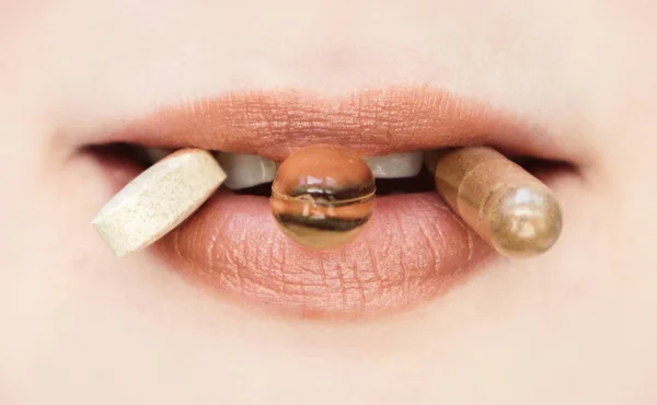 Females mouth in close up with various pills between lips. Happy, low depth of field. Taking vitamins supplements, healthy lifestyle concept.