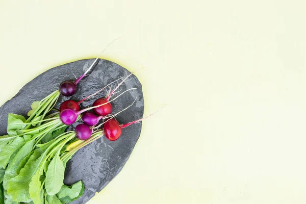 一捆不同颜色的萝卜在一块黑色的石板上 背景是浅黄色的木制 里面有文字 红萝卜 拉法努斯 是一种可食用的根茎蔬菜 — 图库照片