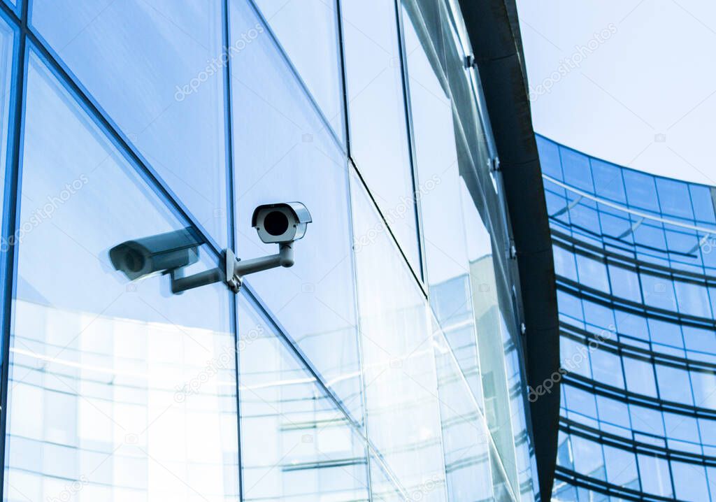 Surveilance camera on modern bank building. Camera reflecting on window.