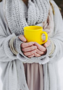 Yumuşak örülmüş kazak giyen Boho kızı kışın dışarıda ve elinde sarı bir bardak sıcak içecek tutuyor. Sığ alan derinliği.