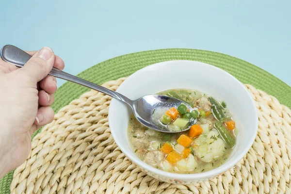 Eating low calories vegetable soup from a white bowl. Hand holding a spoon with soup on it.