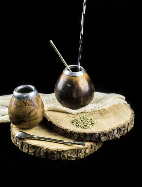 Yerba mate tea calabash with bombilla straw. Pouring water in yerba mate tea calabash mate cups, black background.