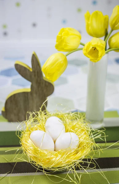 桌上的复活节装饰品 窝里的鸡蛋 白色花瓶里的黄色郁金香 — 图库照片