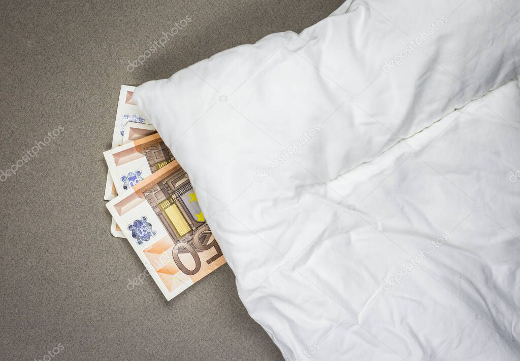 Hiding money under the pillow. 50 euro bank notes under the white pillow.