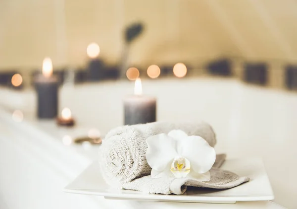 白色瓷盘上有白色兰花的小卷毛巾 在浴室的底座上点着蜡烛 新鲜干洗衣物概念 — 图库照片