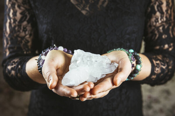 Healer woman holding pure quartz crystal cluster in palms hands. Close up view, using working with crystals concept.