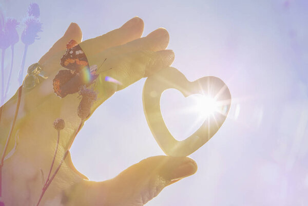 Balance between people and nature concept. Restoring balance in nature. Positive attitude concept. Person holding heart shape, sun star effect on background.