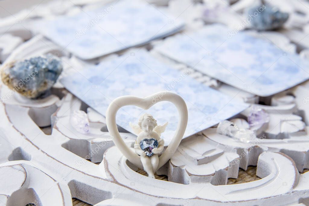 Deck with divination homemade Angel cards on bright white table, surrounded with semi precious stones crystals. Selective focus on cute angel figurine.