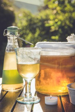 Kombu çayı ve mantarlı kavanoz güneşli yaz akşamlarında açık havada cam kapta servis ediliyor, bahçe, kase içinde kurabiye ve kavanoz şeklinde vazoda beyaz leylak çiçeği..