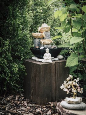 Ağaçlar ve çalılar arasında Buda heykeli olan küçük bir ev bahçesi çeşmesi. Özel zen bahçesi konsepti, modern koyu yeşil renk rötuş.