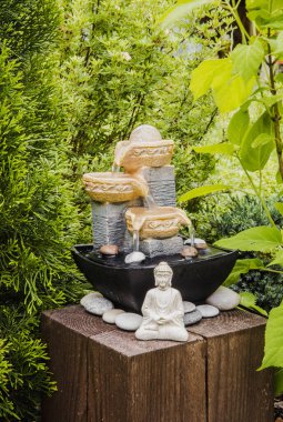 Ağaçlar ve çalılar arasında meditasyon yapan Buda heykeli olan küçük bir ev bahçesi çeşmesi. Özel zen bahçesi konsepti.