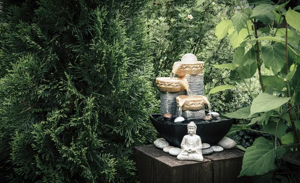 Ağaçlar ve çalılar arasında Buda heykeli olan küçük bir ev bahçesi çeşmesi. Özel zen bahçesi konsepti, modern koyu yeşil renk rötuş.