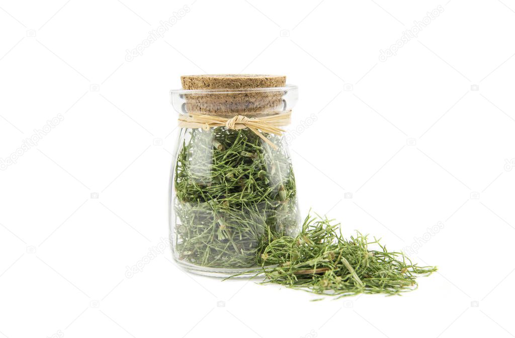 Pile of dried natural herbal medicine called Equisetum arvense the field horsetail or common horsetail isolated on white next to filled glass jar.