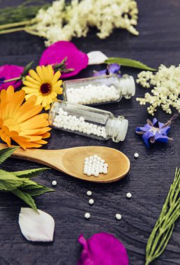 Kaşık üzerindeki Homeopatik İlaç haplarına ve çeşitli bitkilerle süslenmiş tıbbi şişelere odaklanın. Koyu ahşap arka plan..
