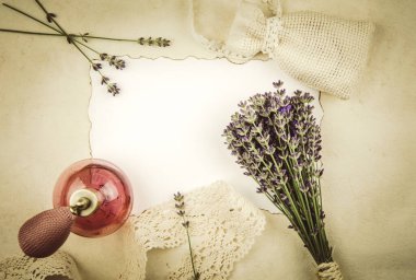 Şirin eski moda pembe sprey parfüm şişesi, kuru lavanta kesesi, arka planda taze lavanta çiçekleri, fotokopi için ortada yanmış kenarları olan boş beyaz kağıt çarşaf..