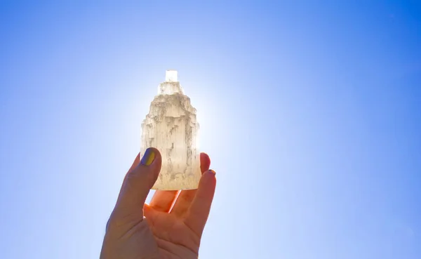 Güneş ve mavi gökyüzüne karşı doğal yontulmuş Selenit kulesi taşıyan kişi taşın iyileştirici ve arındırıcı özellikleri vardır. Ayrıca diğer mineral kristal taşlarını şarj etmek için kullanılır..