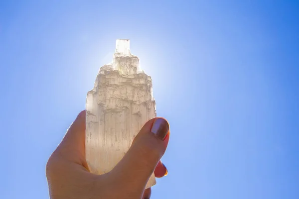 人持有天然雕刻的矿物石硒石塔顶着太阳和蓝天 石材具有治疗和清洁性能 也用于给其他矿物晶体石充电 — 图库照片