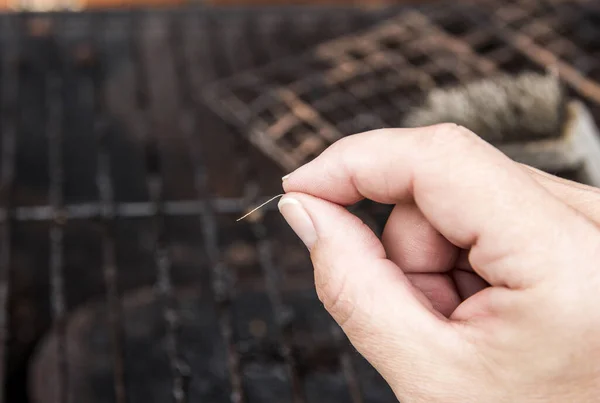 Person hand show loose bristle form bristol grill cleaning brush. Danger when it sticks to meat and person accidentally swallows it. Digestion damage, life threatening situation at home concept.