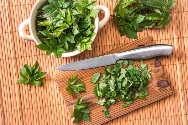 Using fresh young goutweed leaves for food in spring. Aegopodium podagraria commonly called ground elder, herb gerard, bishop\'s weed, gout wort. Chopped leaves on cutting board, preparations.