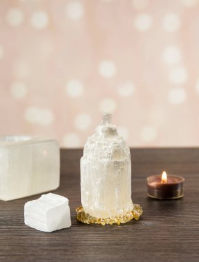 Naturally carved mineral stone Selenite tower has healing on cleansing properties. Candle holder, piece of raw and carved Selenite tower on dark wooden table, orange bokeh background. clipart