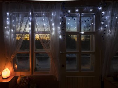 Dekoratif Himalaya Tuz lambası beyaz kumaş perdeleri ile eski beyaz ahşap pencere tarafından yakıldı, orman üzerinde kış aylarında batan ahşap çerçeve penceresinden dışarı baktı. Buzlu cam..