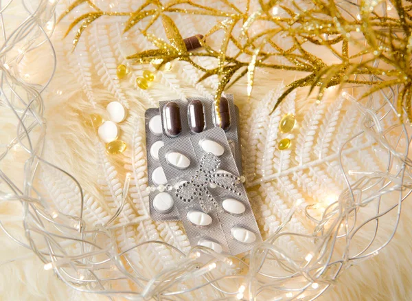Top view of different pills vitamins as a Christmas gift idea concept on white fluffy lambskin with white decorative leaves and party lights. Recovering from Christmas.