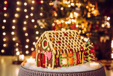 İçinde karamelli cam pencereler ve mum yanan eğlenceli, renkli zencefilli kurabiye evi, arka planda bulanık bokeh Noel ağacı ve oturma odası. Bir sürü kopyalama alanı.