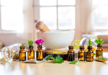  Bitkisel ilaç kompozisyon konsepti. Havan, tokmak ve yapraklarla birlikte gerekli yağ şişeleri. Bulanık beyaz pencere ve parlak bir arka plan. Lavanta, gül, inek ayağı, kadın mantosu, nane şekeri..