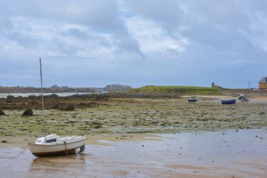 Brittany kıyılarında sular çekildiğinde kum, yosun ve küçük tekneler, bulutlu mavi gökyüzü