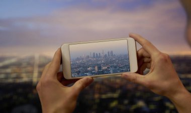 Elleri cep telefonuyla Los Angeles 'ta hava kararırken gökdelenlerin fotoğrafını çekiyor.