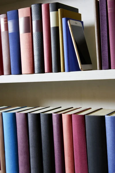 Upright format of bookshelf with new mobile phone standing between colorful book covers , close up, detail