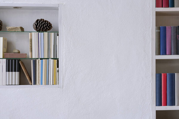 Detail of bookshelves with nice decoration in a white pure plastered wall with copy space
